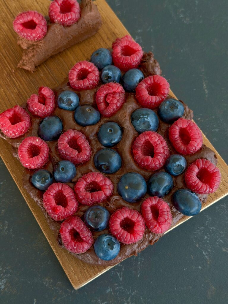 Gesundes Schoko Beeren Dessert auf einem Holzbrett angerichtet mit frischen Himbeeren und Heidelbeeren, cremig angeschnitten mrs flury
