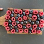 Protein Fudge Gesundes Schoko Beeren Dessert auf einem Holzbrett angerichtet mit frischen Himbeeren und Heidelbeeren, cremig angeschnitten mrs flury