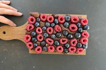 Protein Fudge Gesundes Schoko Beeren Dessert auf einem Holzbrett angerichtet mit frischen Himbeeren und Heidelbeeren, cremig angeschnitten mrs flury