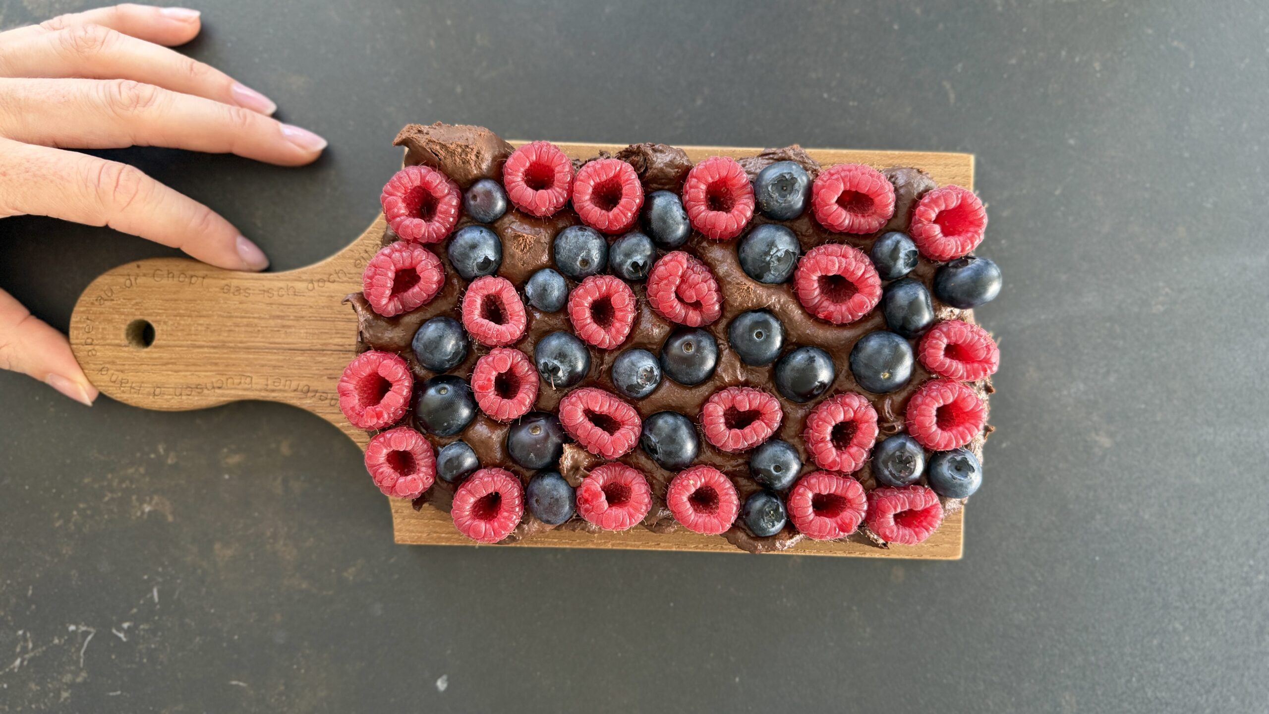 Protein Fudge Gesundes Schoko Beeren Dessert auf einem Holzbrett angerichtet mit frischen Himbeeren und Heidelbeeren, cremig angeschnitten mrs flury